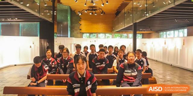 A large group of Zhejiang Wenzhou High School International Division students, wearing their school uniform, attending a lecture or assembly in a wood-paneled auditorium.