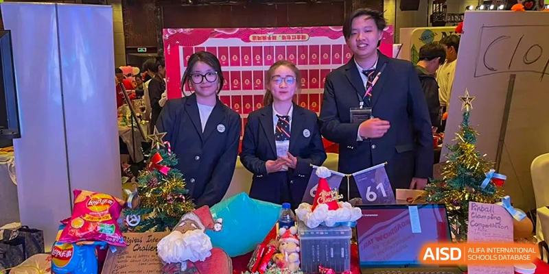 A group of two female students and one male staff member from Zhejiang Wenzhou High School International Division in formal uniforms, posing together at a cheerful, decorated school event.