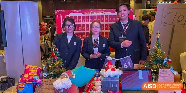 A group of two female students and one male staff member from Zhejiang Wenzhou High School International Division in formal uniforms, posing together at a cheerful, decorated school event.