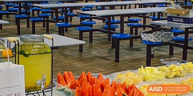 A close-up view of fresh fruit slices, including watermelon and yellow fruit, laid out on a serving counter in the dining area of Zhejiang Wenzhou High School International Division.