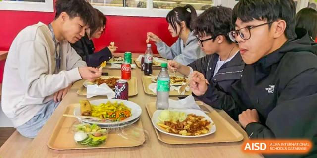 Zhejiang Wenzhou High School International Division students sitting at a wooden table, enjoying a meal of various dishes and bottled drinks.