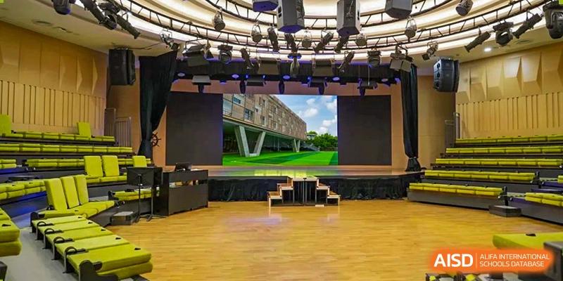 An empty stage and auditorium at YK Pao School with a large screen displaying a building exterior.