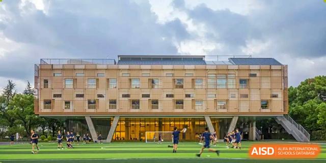 The exterior of a modern YK Pao School building with students playing soccer on a field in the background.
