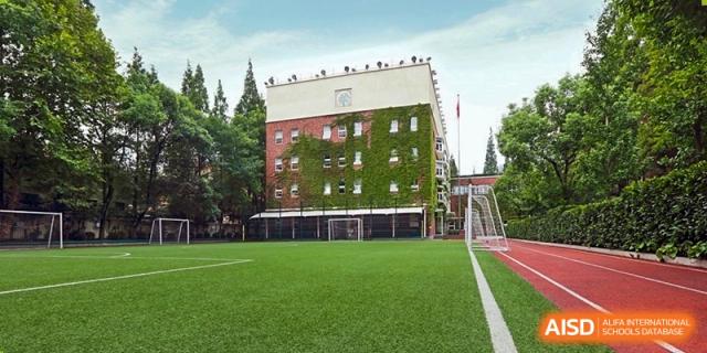 An exterior view of a brick building at YK Pao School with green ivy climbing the walls and a well-maintained sports field in front.