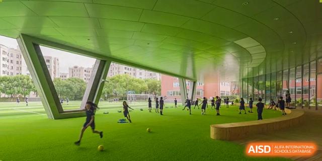 A wide-angle view of students from YK Pao School playing on an outdoor field with a large green canopy overhead.