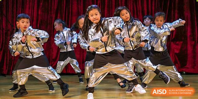 Students from YK Pao School performing a dance in silver jackets and pants on a stage.