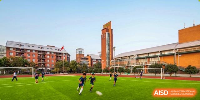 An exterior view of the YK Pao School campus with students playing on the sports field and a bell tower in the background.