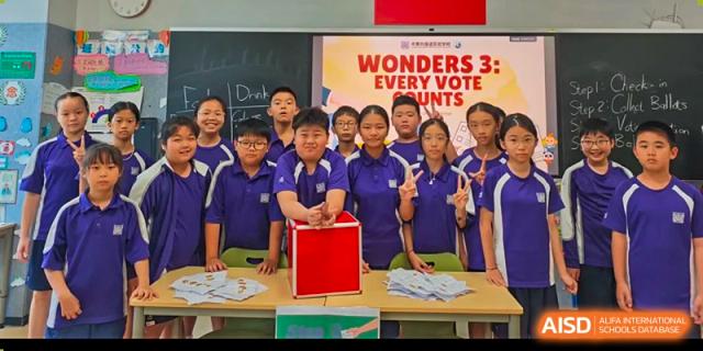 A group of students in a classroom smiles as they pose for a photo with a red box. Guangzhou International Primary/Middle School Huangpu