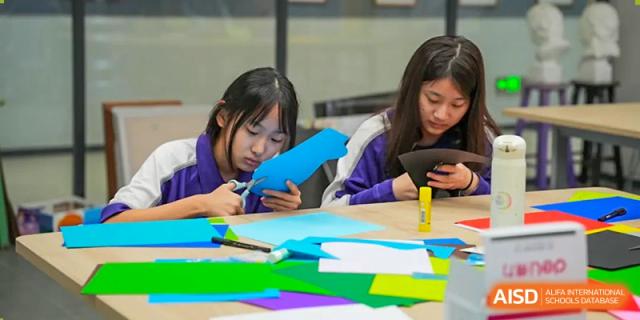 Two female students sit at a desk while doing arts and crafts. Guangzhou International Primary/Middle School Huangpu