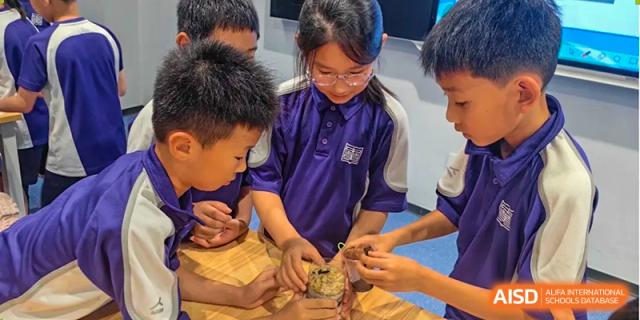 A student in a blue and purple uniform works with a wooden object. Guangzhou International Primary/Middle School Huangpu