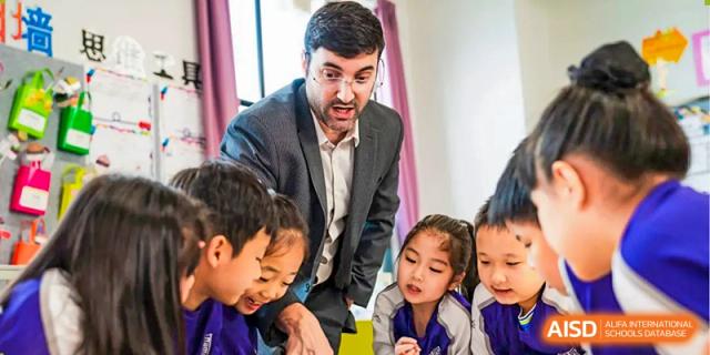 A teacher with a beard talks to a group of young students. Guangzhou International Primary/Middle School Huangpu