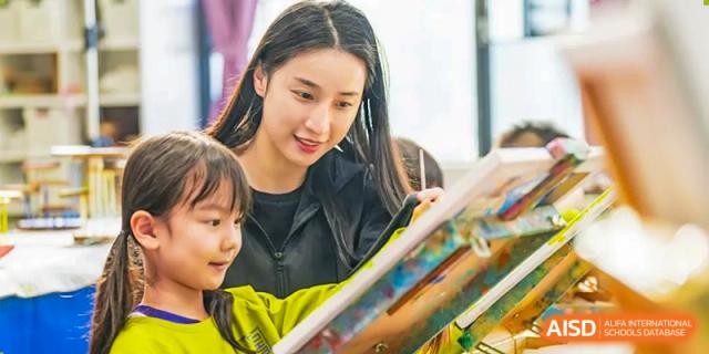A smiling student in a yellow sweater holds two books. Guangzhou International Primary/Middle School Huangpu