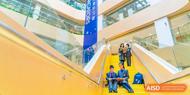 Students in uniform sit on stairs in a school atrium with banners. Guangzhou International Primary/Middle School Huangpu