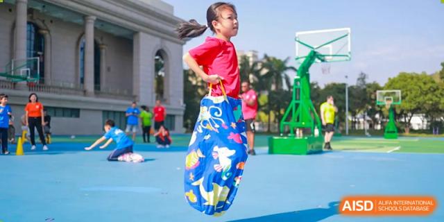 A girl in a red shirt jumps in a sack during a race. Guangzhou International Primary/Middle School Huangpu
