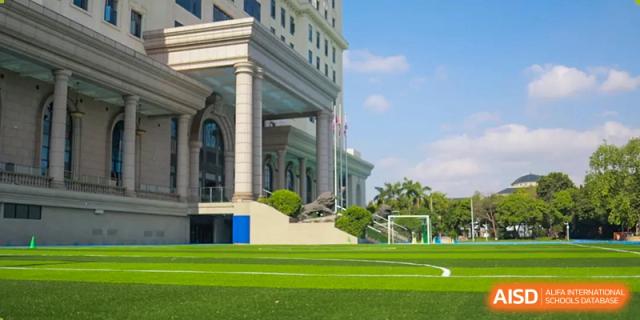 The exterior of a grand, multi-story building next to a green sports field. Guangzhou International Primary/Middle School Huangpu