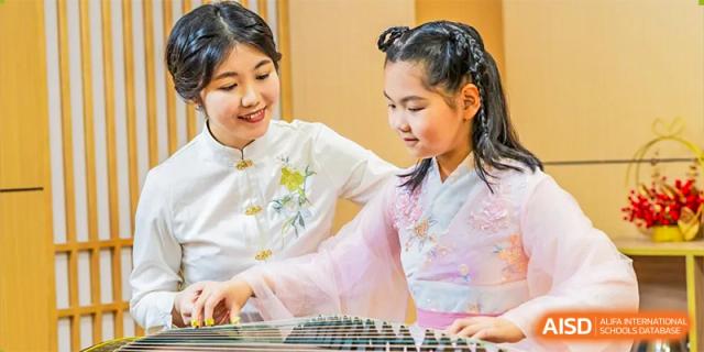 A student in a traditional Chinese outfit smiles while playing an instrument. Guangzhou International Primary/Middle School Huangpu