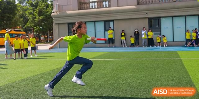 A student in a green jersey runs with a ball during soccer practice. Guangzhou International Primary/Middle School Huangpu