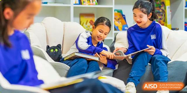 A smiling student in a school uniform sits on a sofa reading a book. Guangzhou International Primary/Middle School Huangpu