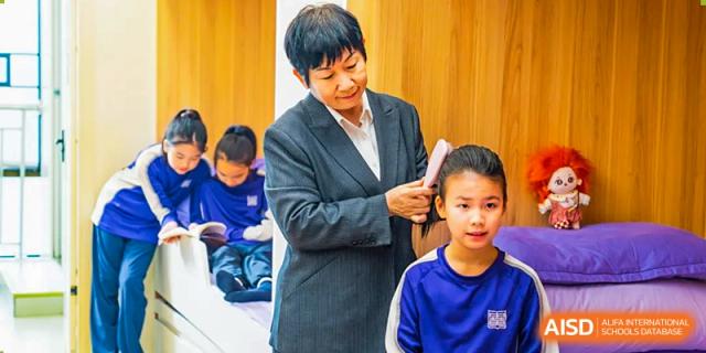 A teacher or staff member with short hair brushes a young student's hair. Guangzhou International Primary/Middle School Huangpu