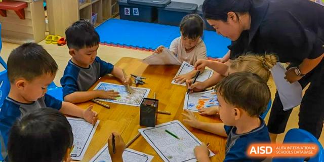 Zhuhai Qiao International School students engage in a group activity, looking at papers and maps around a wooden table.