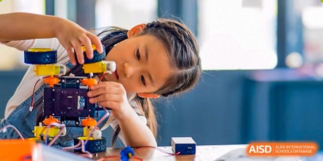A female student at Zhuhai Qiao International School focused intently on a small construction or science project with blocks.