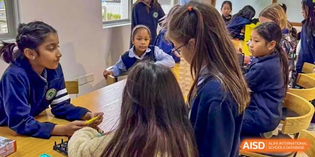Students at Zhuhai Qiao International School collaborating or reviewing documents at a table, with one student's hand pointing at a paper.