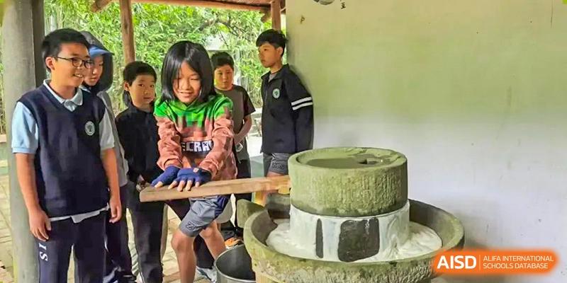 Students from Zhuhai Qiao International School on a field trip, learning to operate a traditional stone grinding mill.