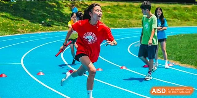 A student from Zhuhai Qiao International School running a race on a bright blue track during a school sports day.