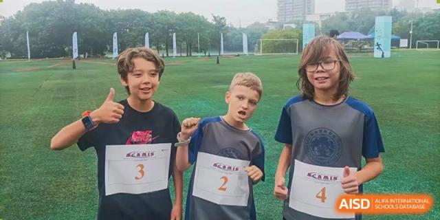 Two students from Zhuhai Qiao International School on the sports field, wearing race numbers after a physical education event.