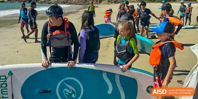 Zhuhai Qiao International School students on a field trip, preparing for a water sport activity like surfing or paddleboarding.