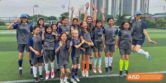 A large group of enthusiastic Zhuhai Qiao International School students in their uniform posing together with their hands raised.