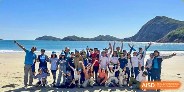 A large group of Zhuhai Qiao International School students and staff posing together for a celebratory photo on a sunny beach.
