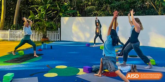 A student or teacher at Zhuhai Qiao International School engaging in an outdoor physical activity or yoga pose on colorful mats, representing Health & Nutrition programs.
