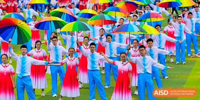 Colorful performance by Chengdu No.7 High School International Department students holding umbrellas and wearing red and blue outfits outdoors.