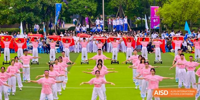 Aerial view of a mass performance by Chengdu No.7 High School International Department students in pink outfits performing on a field with red ground cover.