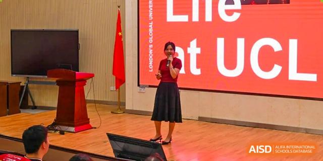 Chengdu No.7 High School International Department speaker presenting on a stage in front of a large red screen and the Chinese flag.