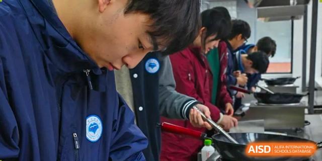 Close-up of a focused Chengdu No.7 High School International Department student stirring food in a pan during a cooking or nutrition class.