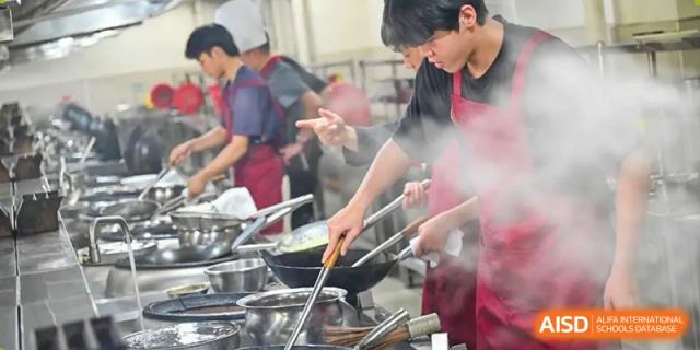 Chengdu No.7 High School International Department students wearing aprons and actively cooking on stovetops during a culinary arts or nutrition lesson.