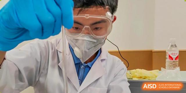 A Chengdu Shishi High School Cambridge A-Level Centre student in a lab coat and goggles works with a pipette.