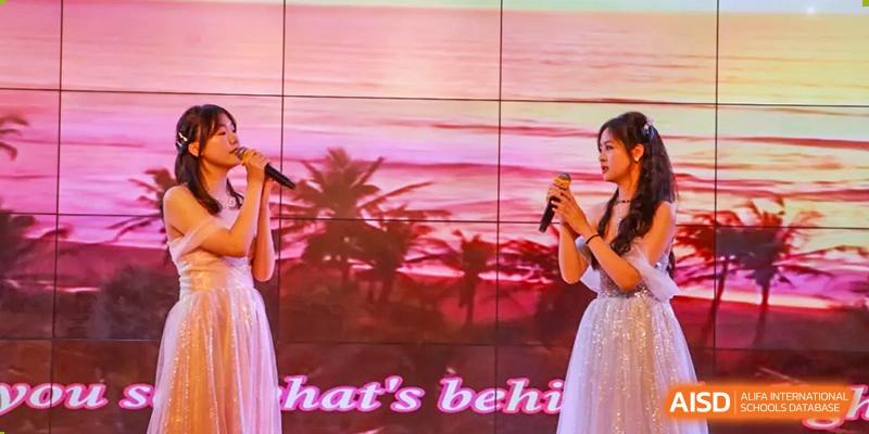 Chengdu Shishi High School Cambridge A-Level Centre students perform on a stage with a screen displaying text behind them.
