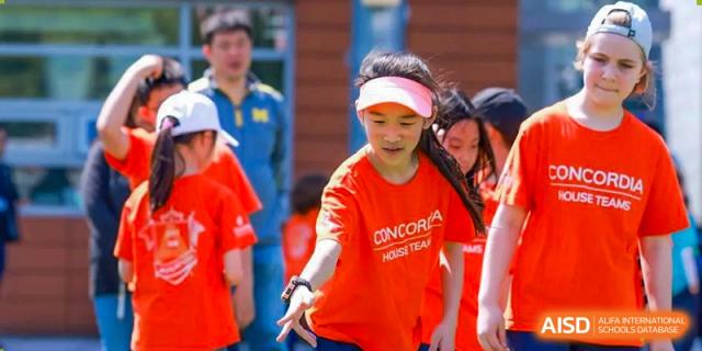 A female student from Concordia International School Shanghai, wearing an orange shirt and sun visor, participating in a frisbee activity on a sports field.
