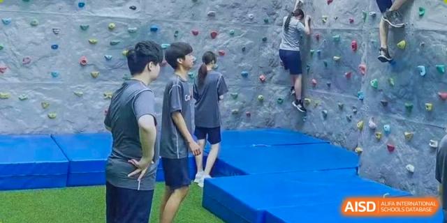 Concordia International School Shanghai students standing near a climbing wall, with one student starting to climb on the right.