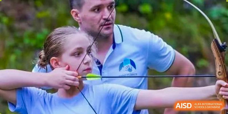 A young Concordia International School Shanghai student learning archery with a bow and arrow under the supervision of a coach.