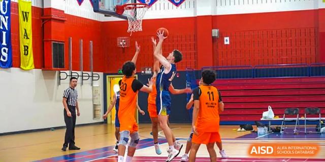 Three Concordia International School Shanghai students jumping near the basket in an attempt to score or block during a basketball game.