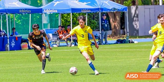 A male Concordia International School Shanghai student in a yellow uniform dribbling a soccer ball on a turf field.
