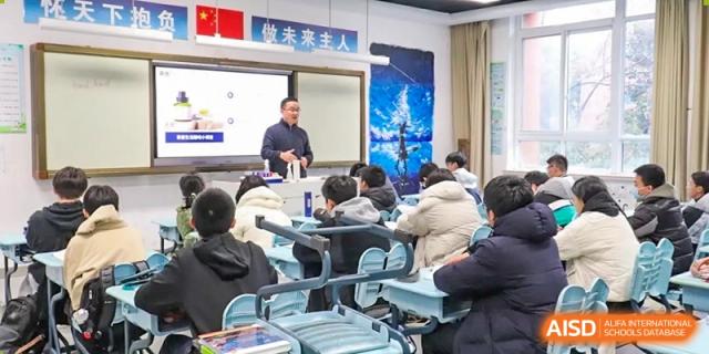 A male teacher leading a discussion or presentation from the front of a modern classroom to engaged students at the Hefei No.1 High School.