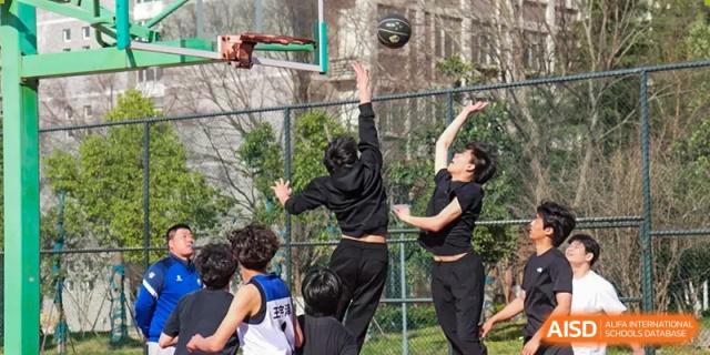 Students playing basketball outdoors, with one student leaping to shoot a jump shot at the Hefei No.1 High School.