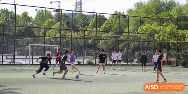 A group of students playing a football match on a fenced turf field under sunny skies at the Hefei No.1 High School.