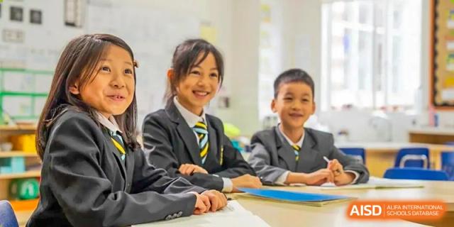 Two happy students in uniform collaborating at a desk in a classroom at Hiba Academy Hangzhou.