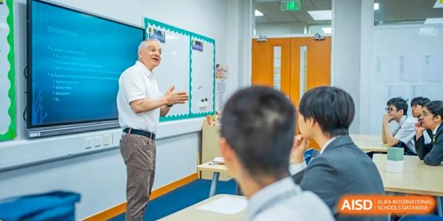 Two adults discussing a topic with a group of students in a bright classroom setting at Hiba Academy Hangzhou.